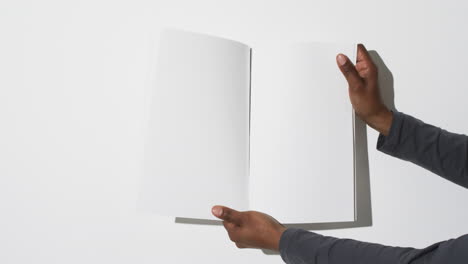 Video-of-hand-of-african-american-man-holding-book-with-blank-pages,-copy-space-on-white-background