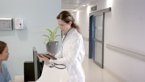 Diverse-female-doctors-using-tablet-and-computer-at-hospital-reception-desk,-copy-space,-slow-motion