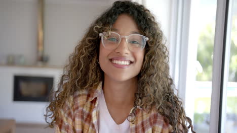 Portrait-of-happy-biracial-female-teenager-with-curly-hair-at-home,-slow-motion