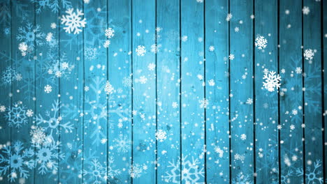 Animation-of-snow-falling-on-blue-wooden-background-with-copy-space-at-christmas
