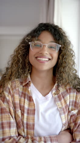 Vertical-video-of-portrait-of-happy-biracial-female-teenager-with-curly-hair-at-home,-slow-motion