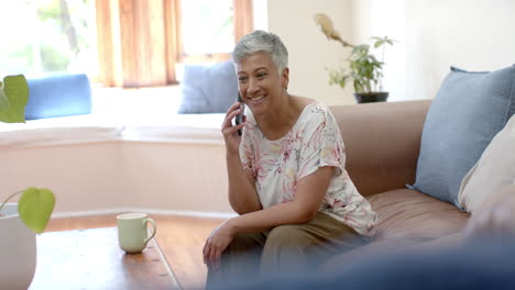 Glückliche-ältere-Frau-Mit-Gemischter-Abstammung,-Die-Auf-Der-Couch-Sitzt-Und-Zu-Hause-Mit-Dem-Smartphone-Spricht,-Zeitlupe