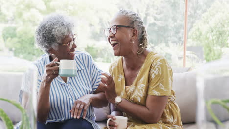 Glückliche-ältere-Afroamerikanische-Freundinnen,-Die-Kaffee-Trinken-Und-Im-Wohnzimmer-Lachen,-Zeitlupe