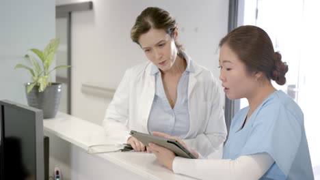 Focused-diverse-female-doctors-using-tablet-and-discussing-at-hospital-reception-desk,-slow-motion