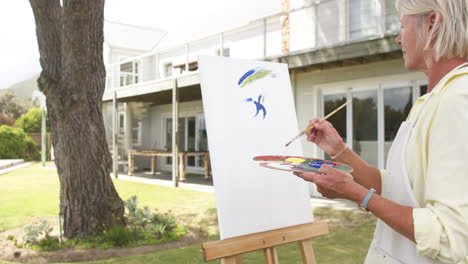 Happy-caucasian-senior-woman-painting-picture-and-smiling-in-sunny-garden,-slow-motion
