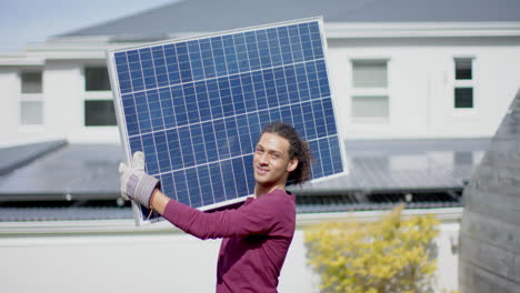 Portrait-of-happy-biracial-man-with-gloves-carrying-solar-panel-in-garden,-slow-motion