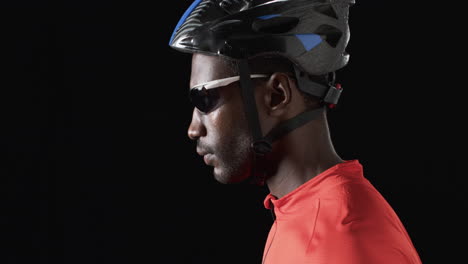 African-American-cyclist-in-cycling-gear-poses-confidently-on-a-black-background,-with-copy-space
