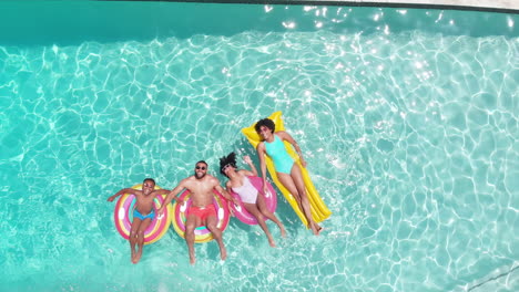 Aerial-of-african-american-parents,-son-and-daughter-lying-on-inflatables-in-sunny-pool,-copy-space