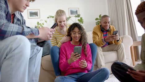 Happy-diverse-group-of-teenage-friends-using-smartphones-and-laughing-at-home,-slow-motion
