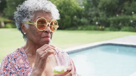 Happy-senior-african-american-woman-in-sunglasses-by-pool-drinking-cocktail,-copy-space,-slow-motion