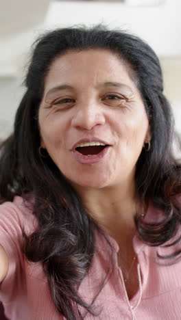 Feliz-Mujer-Mayor-Birracial-Teniendo-Videollamada-Y-Sonriendo-En-Una-Habitación-Soleada,-Cámara-Lenta