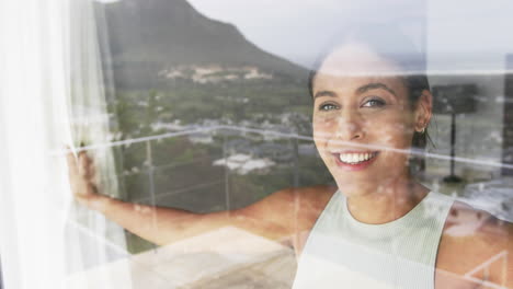 Portrait-of-happy-biracial-woman-looking-through-window-at-home,-slow-motion