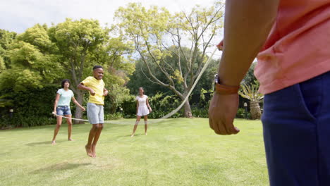 Glückliche-Afroamerikanische-Eltern,-Sohn-Und-Tochter-Hüpfen-Im-Sonnigen-Garten,-Zeitlupe