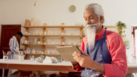 Happy-biracial-potter-with-long-beard-using-tablet-and-smiling-in-pottery-studio,-slow-motion