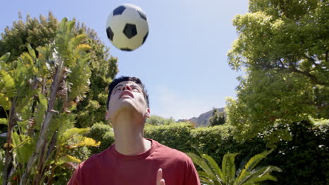Biracial-man-practicing-skills-heading-football-in-sunny-garden,-copy-space,-slow-motion