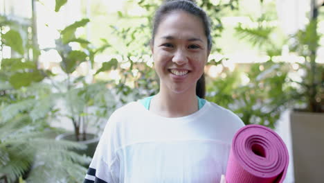 Happy-asian-woman-with-exercise-mat-smiling-on-sunny-terrace,-slow-motion