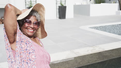 Glückliche-ältere-Afroamerikanische-Frau-Mit-Sonnenhut,-Die-Auf-Der-Terrasse-In-Der-Sonne-Sitzt,-Kopierraum,-Zeitlupe