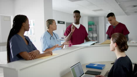 Diverse-male-and-female-doctors-discussing-work-at-reception-desk-at-hospital,-slow-motion