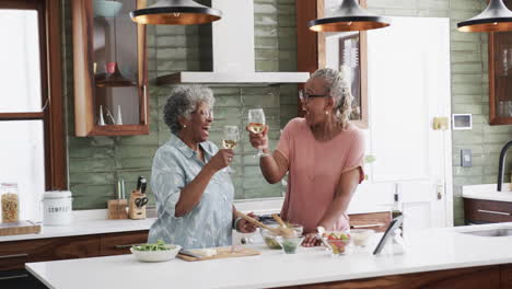 Senior-african-american-female-friends-cooking-and-drinking-wine-in-kitchen,-copy-space,-slow-motion