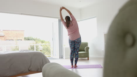 Rear-view-of-plus-size-biracial-woman-practicing-yoga-standing,-stretching,-copy-space,-slow-motion