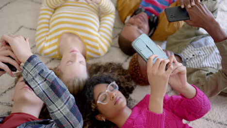 Fröhliche,-Vielfältige-Gruppe-Von-Teenager-Freunden,-Die-Smartphones-Benutzen-Und-Zu-Hause-Auf-Dem-Teppich-Liegen,-Zeitlupe