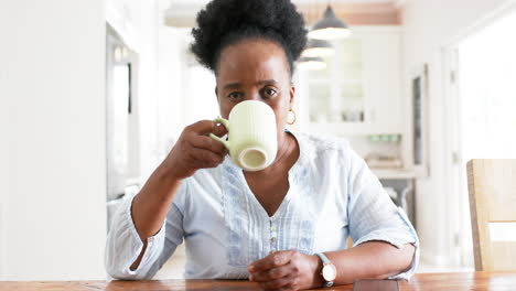 African-american-senior-woman-having-video-call-and-drinking-from-cup-in-sunny-room,-slow-motion