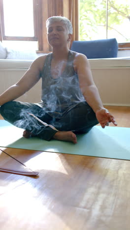 Vertical-video-of-focused-senior-biracial-woman-meditating-with-incense-sticks-at-home,-slow-motion