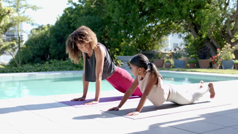 Happy-biracial-mother-and-daughter-practicing-yoga-pose-in-sunny-garden,-slow-motion