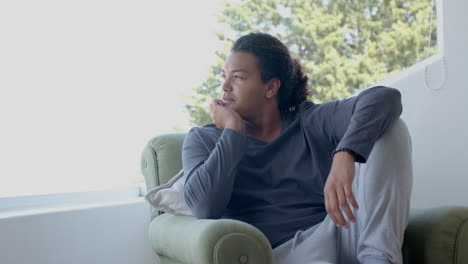 Happy,-thoughtful-biracial-man-sitting-in-sunny-living-room-enjoying-view,-copy-space,-slow-motion