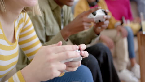 Happy-diverse-group-of-teenage-friends-sitting-on-couch-and-playing-video-games-at-home,-slow-motion