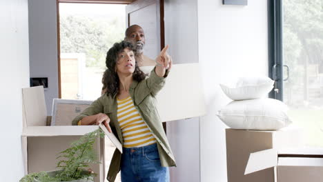 Happy-biracial-couple-talking-and-carrying-cartons-at-new-house,-slow-motion