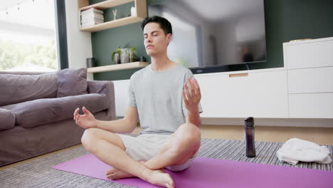 Biracial-man-practicing-yoga-meditation-and-breathing-sitting-on-floor,-copy-space,-slow-motion