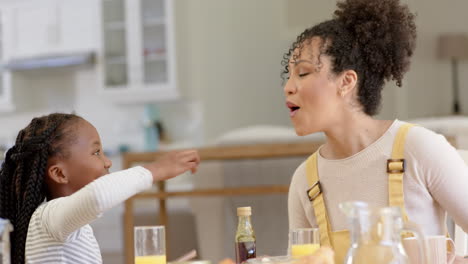 Happy-african-american-mother-and-daughter-having-breakfast-and-feeding-at-home,-slow-motion