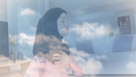 Animation-of-clouds-over-biracial-woman-in-hijab-practicing-yoga