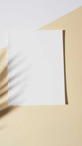 Vertical-video-of-shadow-over-book-with-blank-pages-and-copy-space-on-yellow-background