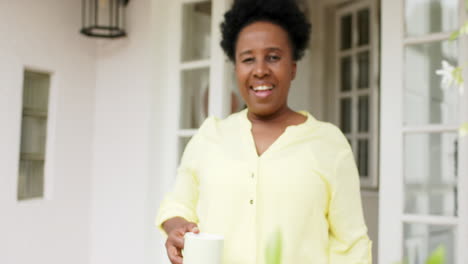 Happy-african-american-senior-woman-walking-with-cup-smiling-outside-house,-slow-motion
