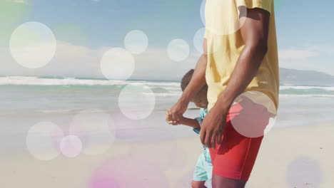 Animation-Von-Lichtpunkten-über-Einem-Glücklichen-Afroamerikanischen-Vater-Und-Sohn,-Die-Am-Strand-Spazieren-Gehen