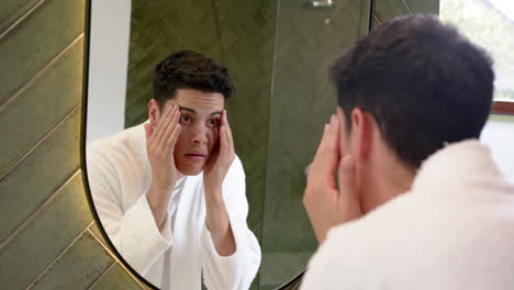 Focused-biracial-man-inspecting-face-in-bathroom-mirror,-slow-motion