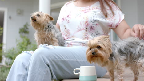 Happy-plus-size-biracial-woman-sitting-in-garden-petting-her-dogs,-slow-motion
