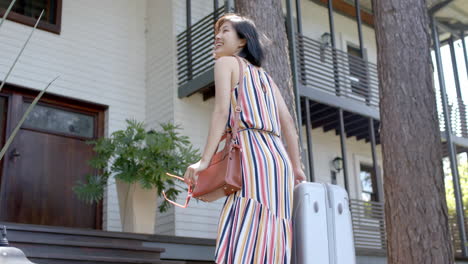 Happy-asian-woman-with-suitcase-walking-on-stairs-of-home-on-sunny-day,-slow-motion