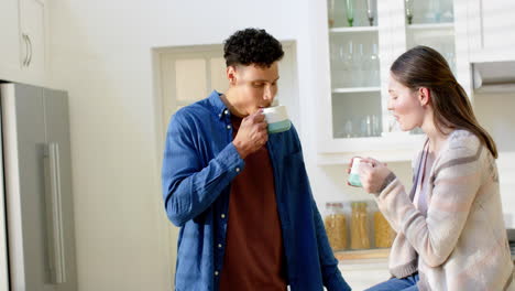 Happy-diverse-couple-talking-and-drinking-coffee-in-kitchen-at-home,-in-slow-motion