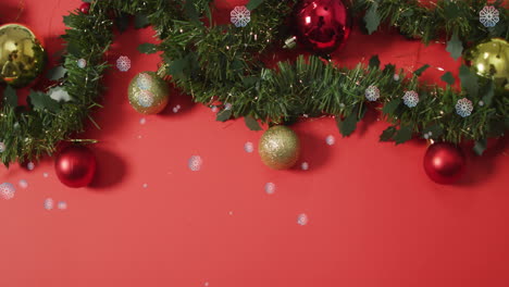 Animation-of-snow-falling-over-christmas-tree-with-baubles-on-red-background