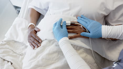 Hands-of-diverse-female-doctor-and-senior-female-patient-in-bed-in-hospital-room,-slow-motion