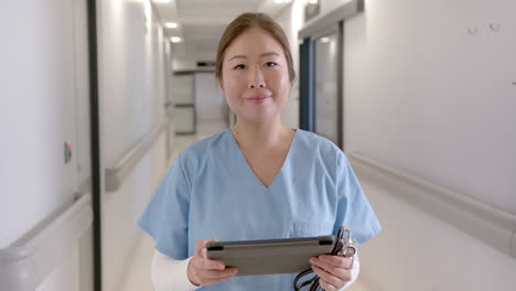 Retrato-De-Una-Feliz-Doctora-Asiática-Con-Tableta-Sonriendo-En-El-Pasillo-Del-Hospital,-Cámara-Lenta
