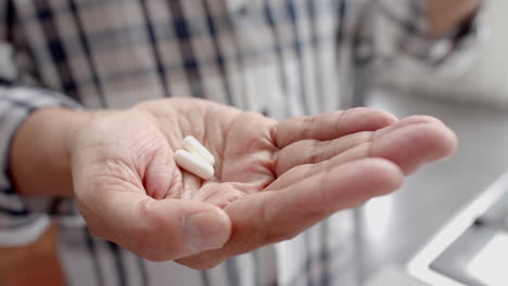 Midsection-of-senior-biracial-man-at-home-holding-two-pills-in-palm-of-hand,-slow-motion