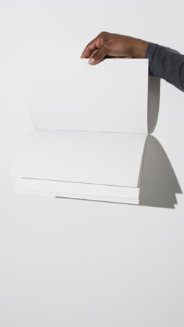 Vertical-video-of-hand-of-african-american-man-with-book-with-white-blank-pages-on-white-background