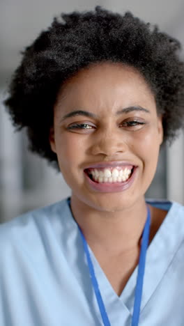 Vertical-video-of-portrait-of-happy-african-american-female-doctor-in-hospital-corridor,-slow-motion