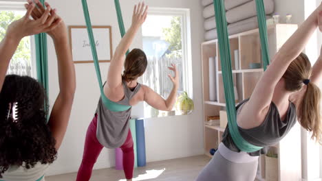 Focused-diverse-fitness-teenage-girls-in-aerial-yoga-class-in-big-white-room,-slow-motion