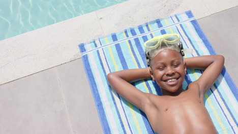 High-angle-of-happy-african-american-boy-in-goggles-sunbathing-by-pool,-copy-space,-slow-motion