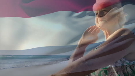 Animation-of-flag-of-the-netherlands-over-senior-caucasian-woman-on-beach